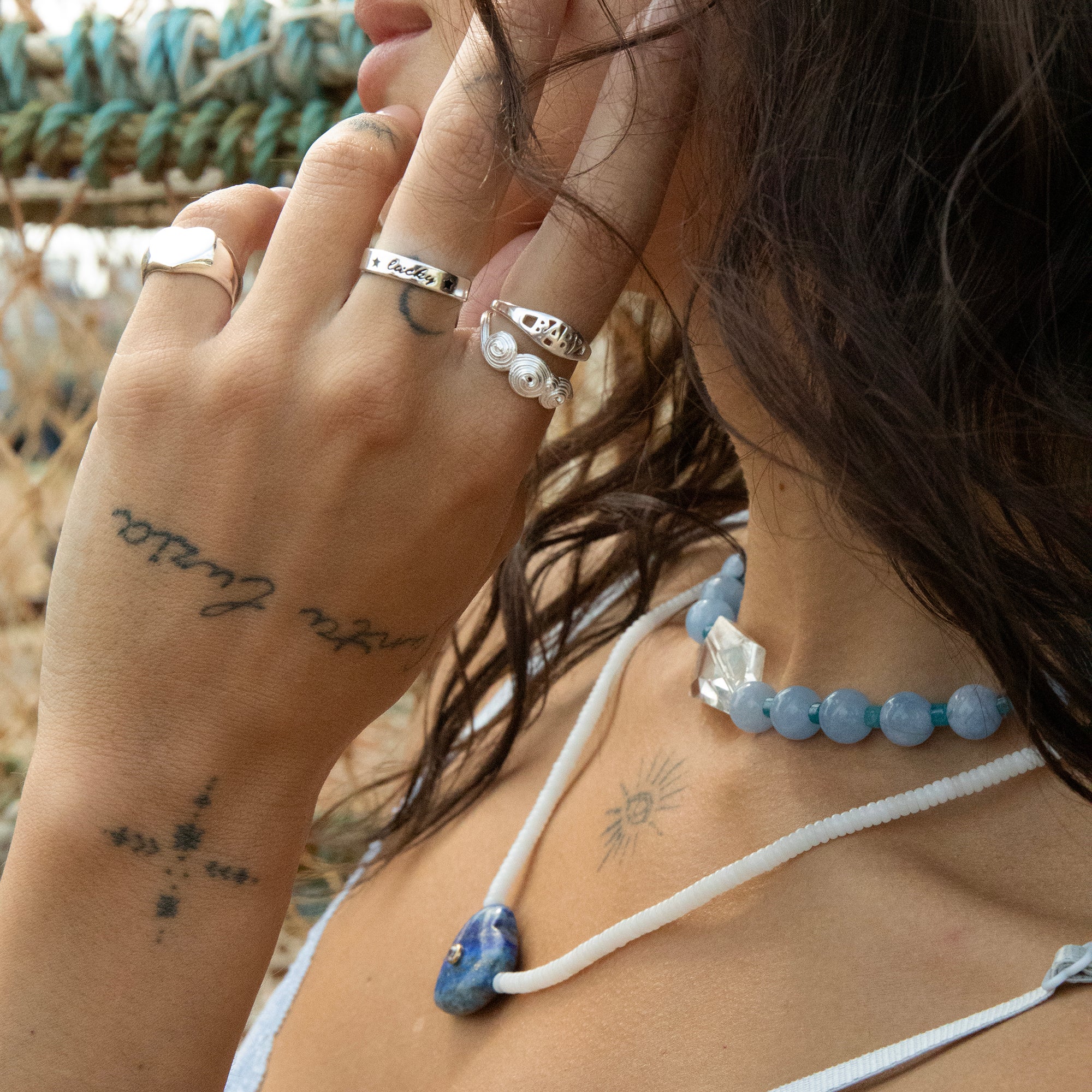 Close-up of a person wearing multiple rings and a necklace with a blurred natural background - silver lucky ring - seolgold
