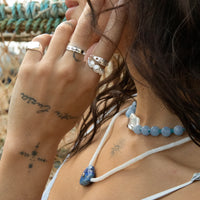 Close-up of a person wearing multiple rings and a necklace with a blurred natural background - silver lucky ring - seolgold