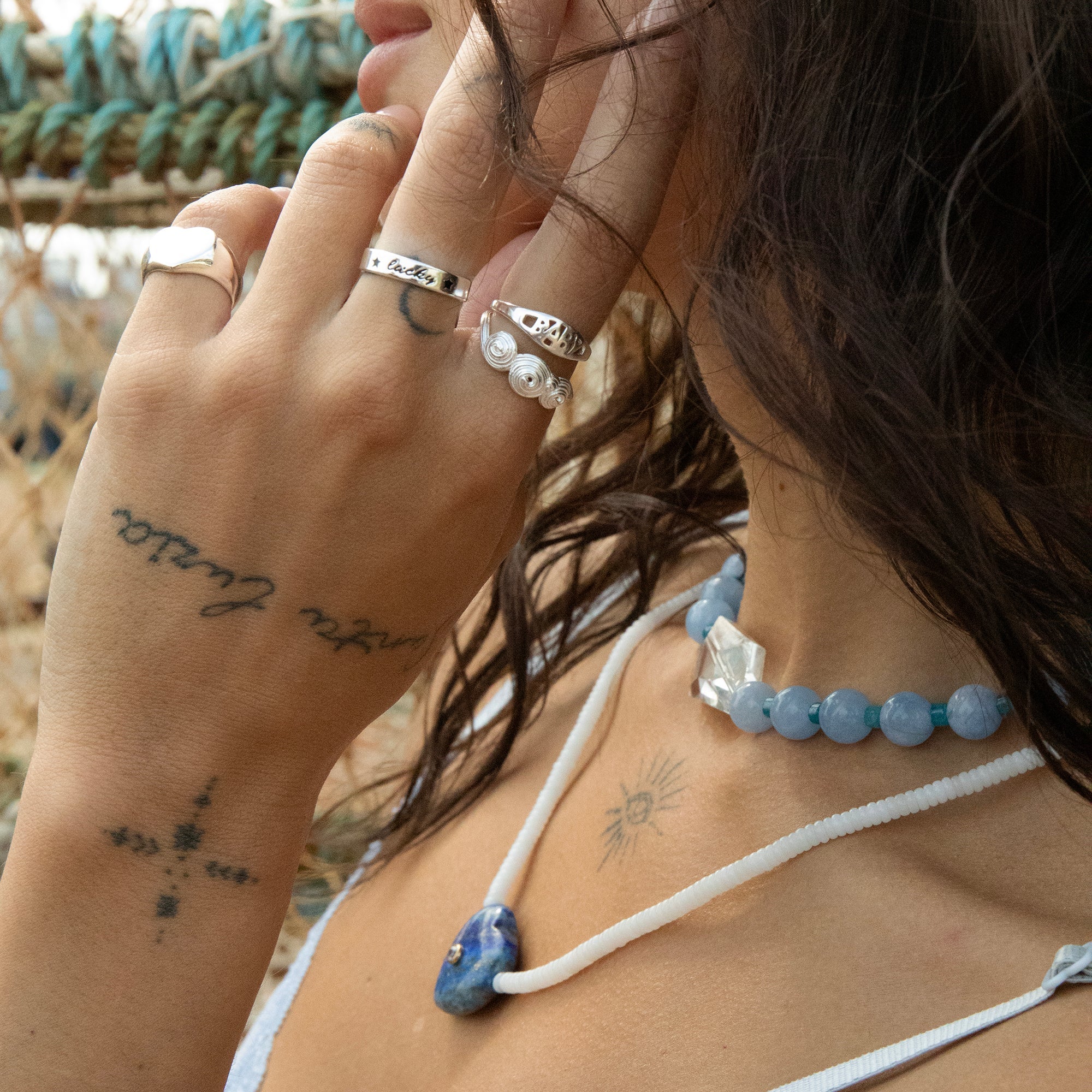 Close-up of a person wearing multiple rings and a necklace with a blurred natural background - seolgold