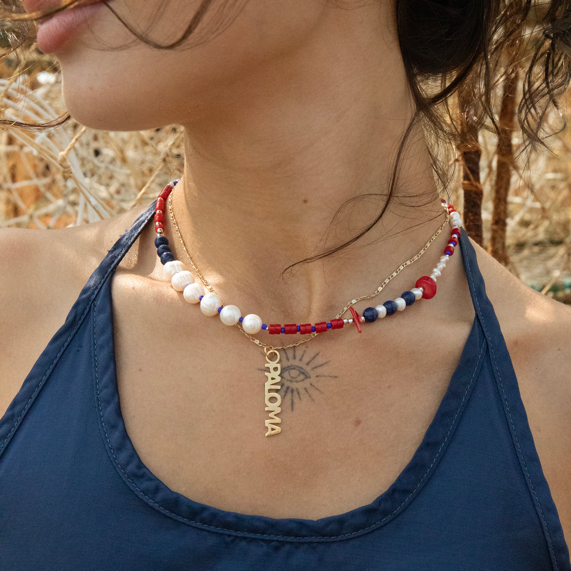 Close-up of a person wearing a beaded necklace with 'nameplate' pendant outdoors - seolgold