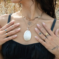 Person wearing a necklace with a shell pendant, surrounded by natural elements - seolgold