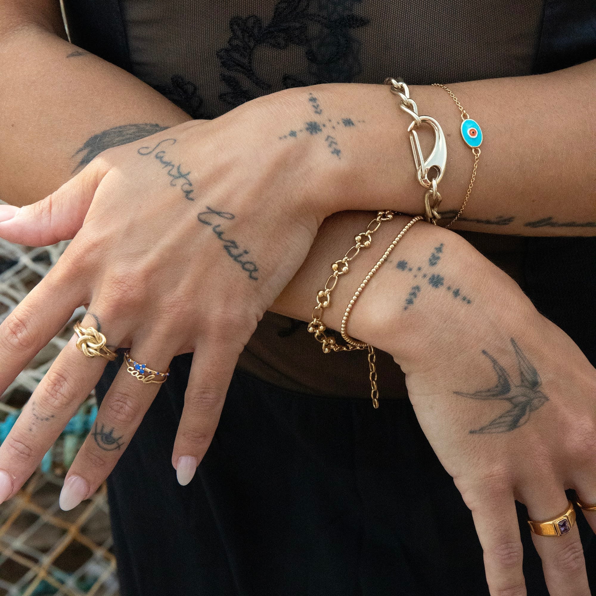 Close-up of hands with gold jewelry and tattoos on a blurred background - caribener bracelet - seolgold