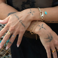 Close-up of hands with gold jewelry and tattoos on a blurred background - caribener bracelet - seolgold