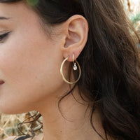 Close-up of a woman's ear wearing gold hoop earrings with a blurred natural background - solid gold hoops - large 9ct gold hoops - seolgold
