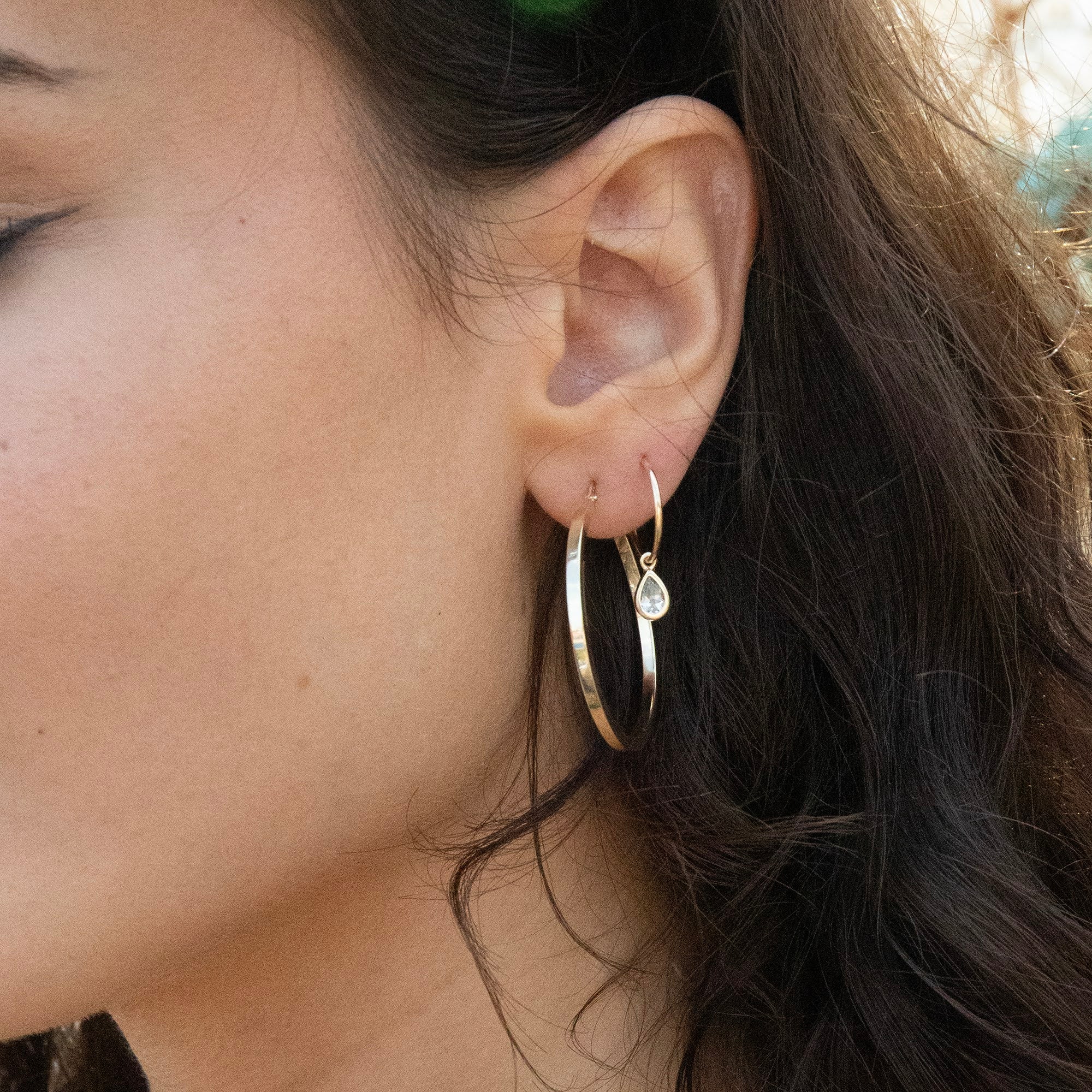 Close-up of a person wearing gold hoop earrings with a blurred background - solid gold hoops - large 9ct gold hoops - seolgold