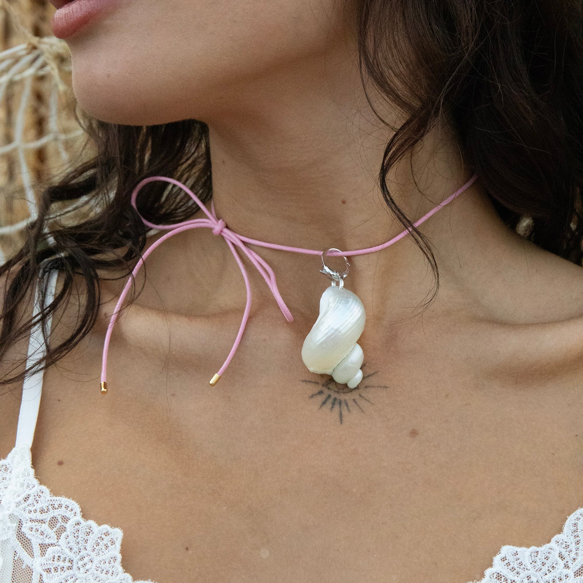 Close-up of a necklace with a large white stone pendant on a person wearing a white lace top - pink cord necklace - pink cord shell necklace - seolgold