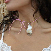 Close-up of a necklace with a large white stone pendant on a person wearing a white lace top - pink cord necklace - pink cord shell necklace - seolgold