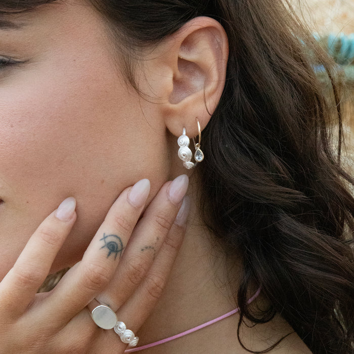 Close-up of a woman wearing pearl earrings and a ring, with a blurred background - seolgold