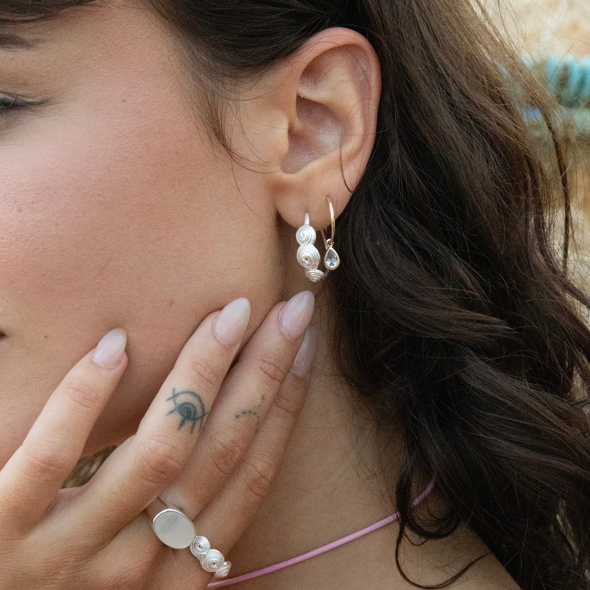 Close-up of a woman wearing pearl earrings and a ring, with a blurred background - seolgold