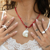 Person wearing a red beaded necklace with a shell pendant, surrounded by hands with starfish rings - seolgold