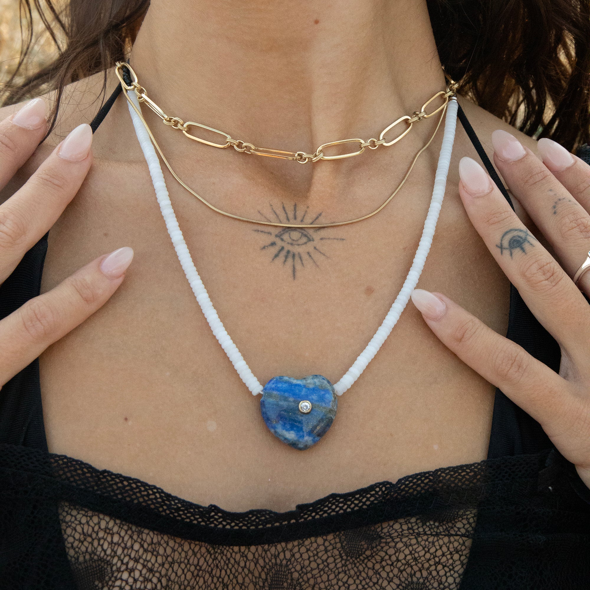 Person wearing a gold chain necklace with a blue heart-shaped pendant, hands visible - seolgold