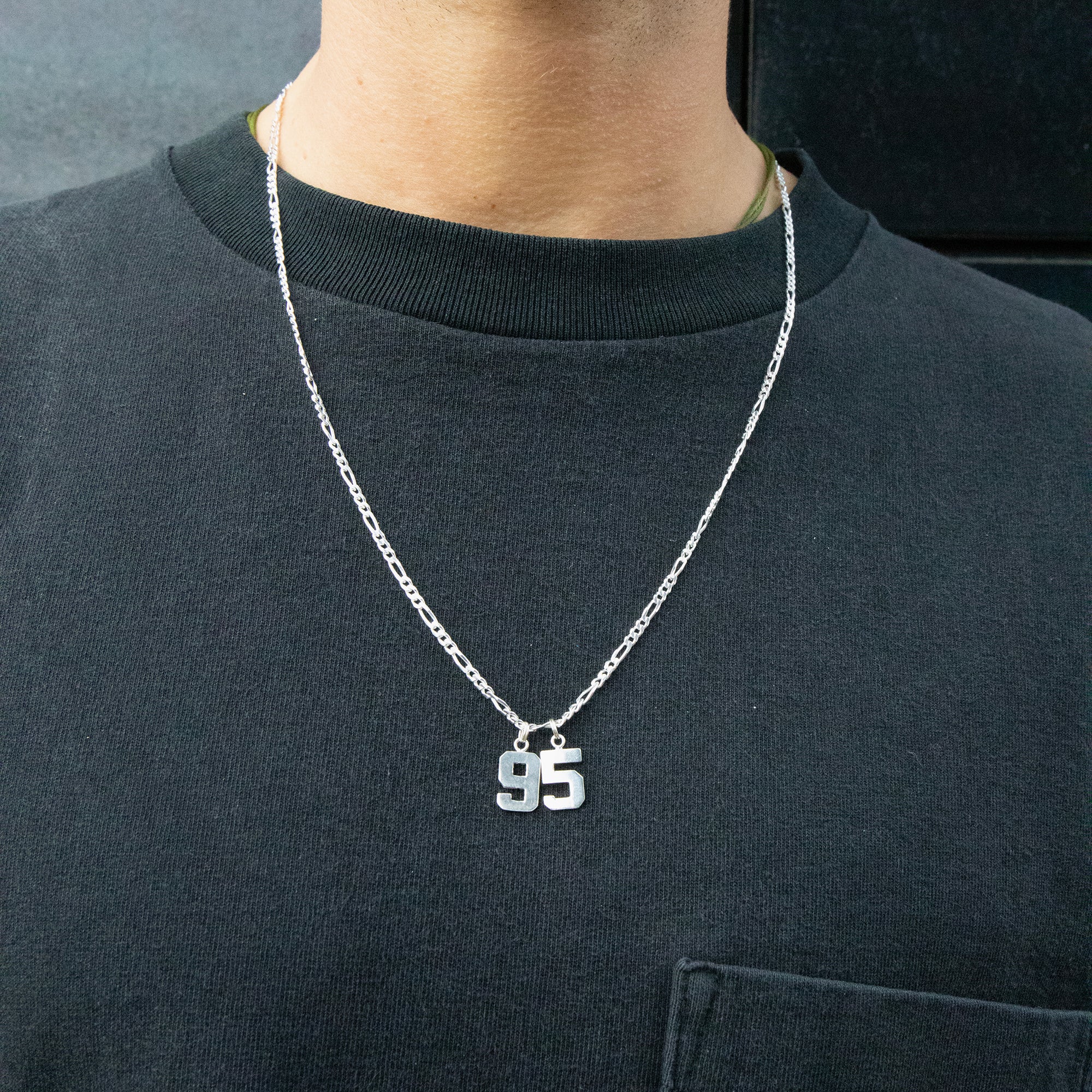 Person wearing a black shirt with a silver necklace featuring the number '95' - seolgold