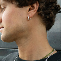 Close-up of a person wearing a silver hoop earring with a blurred background - seolgold