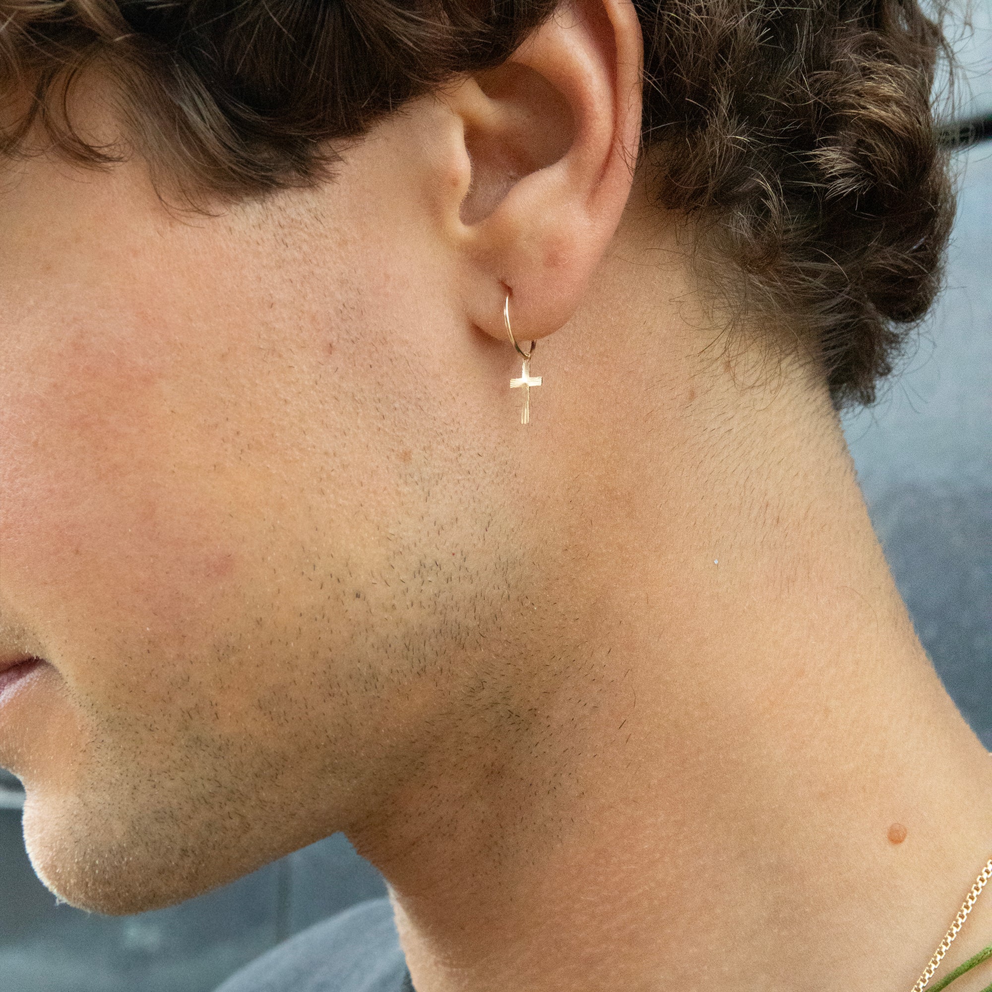 Close-up of a person wearing a gold hoop earring with a cross design - seolgold