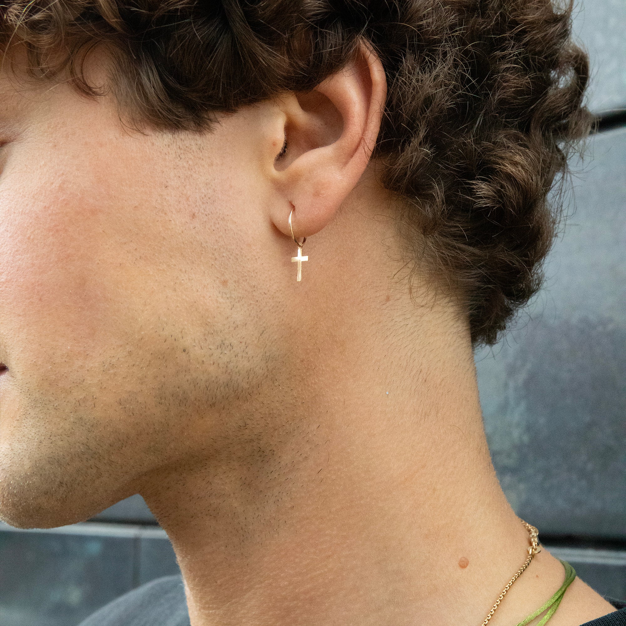 Close-up of a person wearing a gold cross earring with a blurred background - seolgold