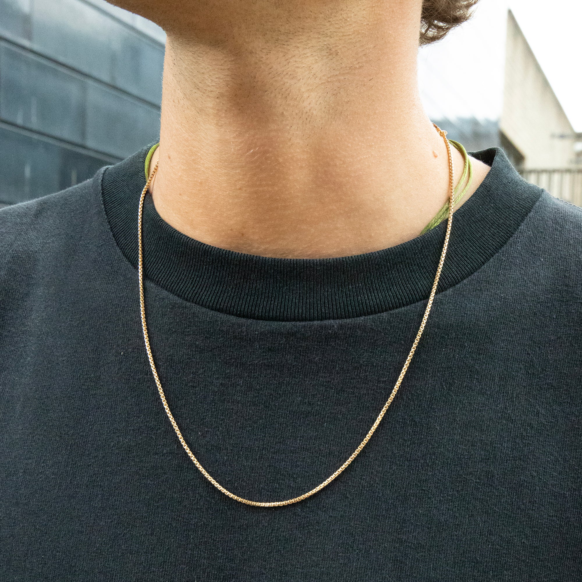 Person wearing a gold chain necklace with a blurred background - seolgold