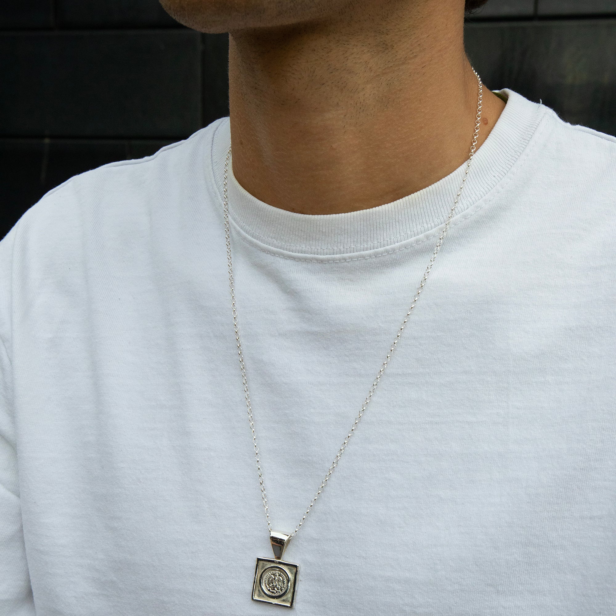 Person wearing a silver necklace with a pendant on a plain background - seolgold