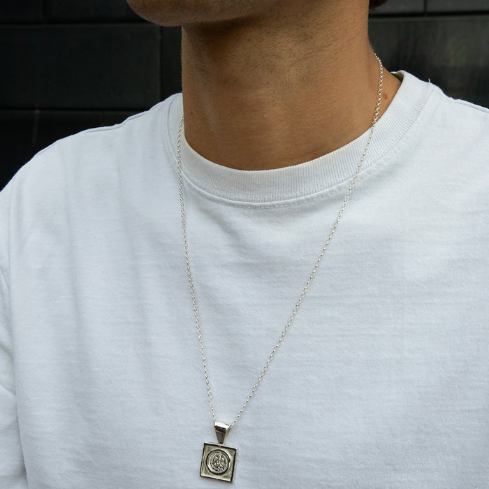 Person wearing a silver necklace with a pendant on a plain background - seolgold