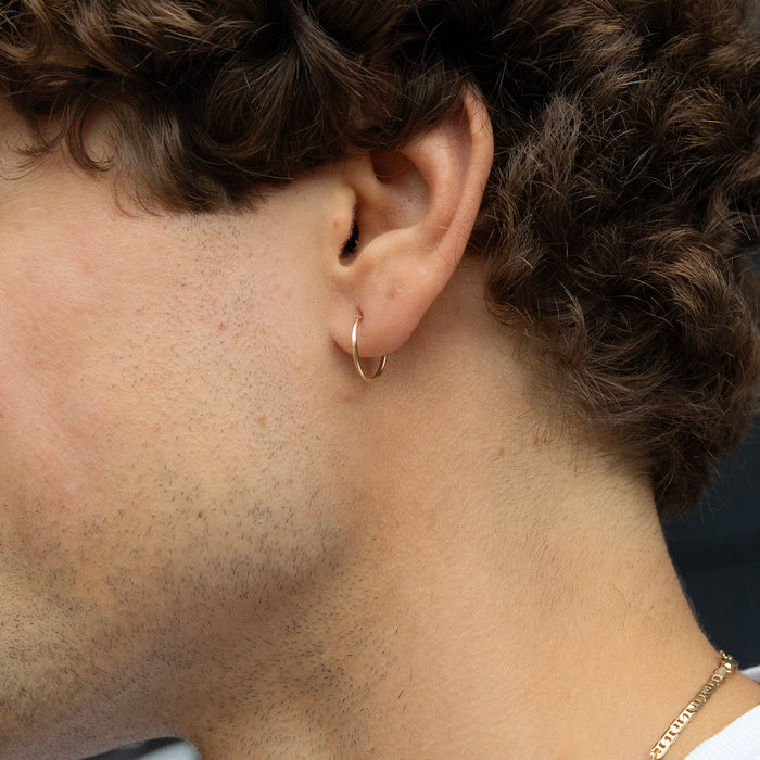 Close-up of an ear wearing a gold hoop earring with a blurred background - seolgold