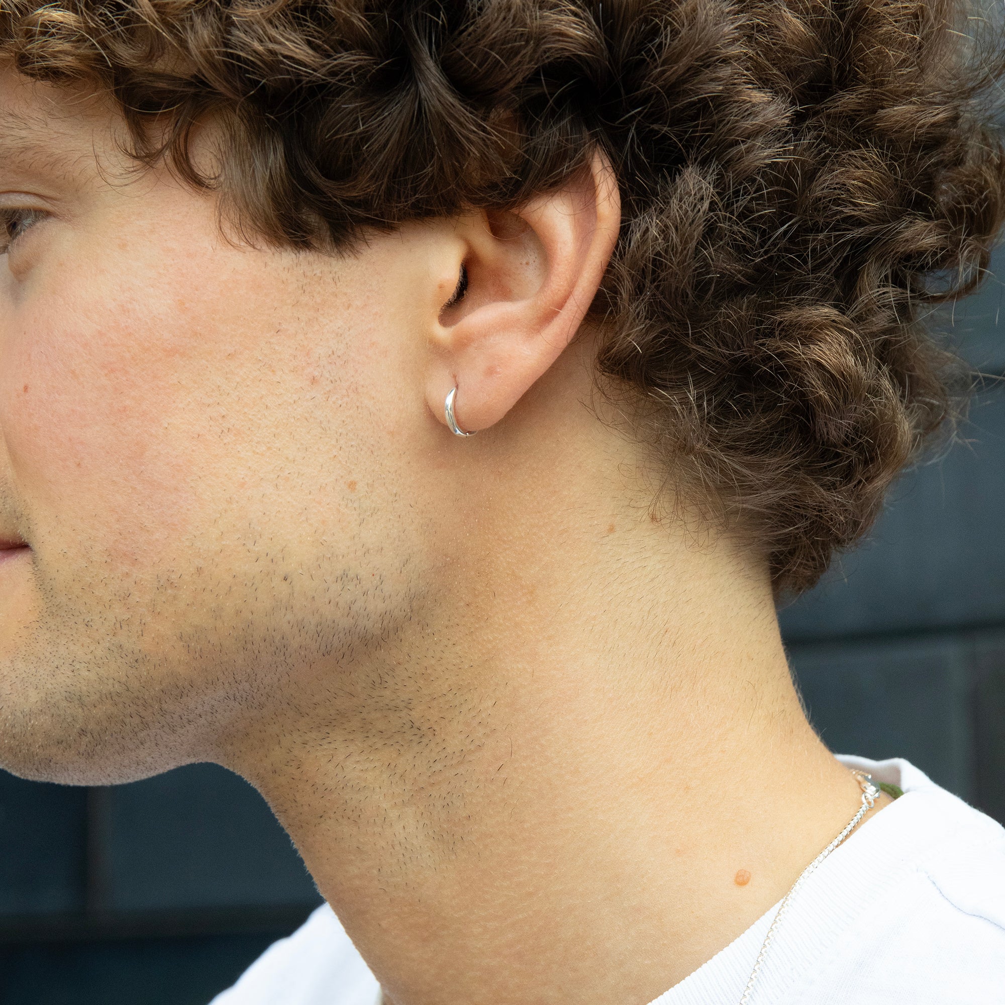 Close-up of a person wearing a silver hoop earring with a blurred background - tiny silver earring - mens silver hoop earring - seolgold