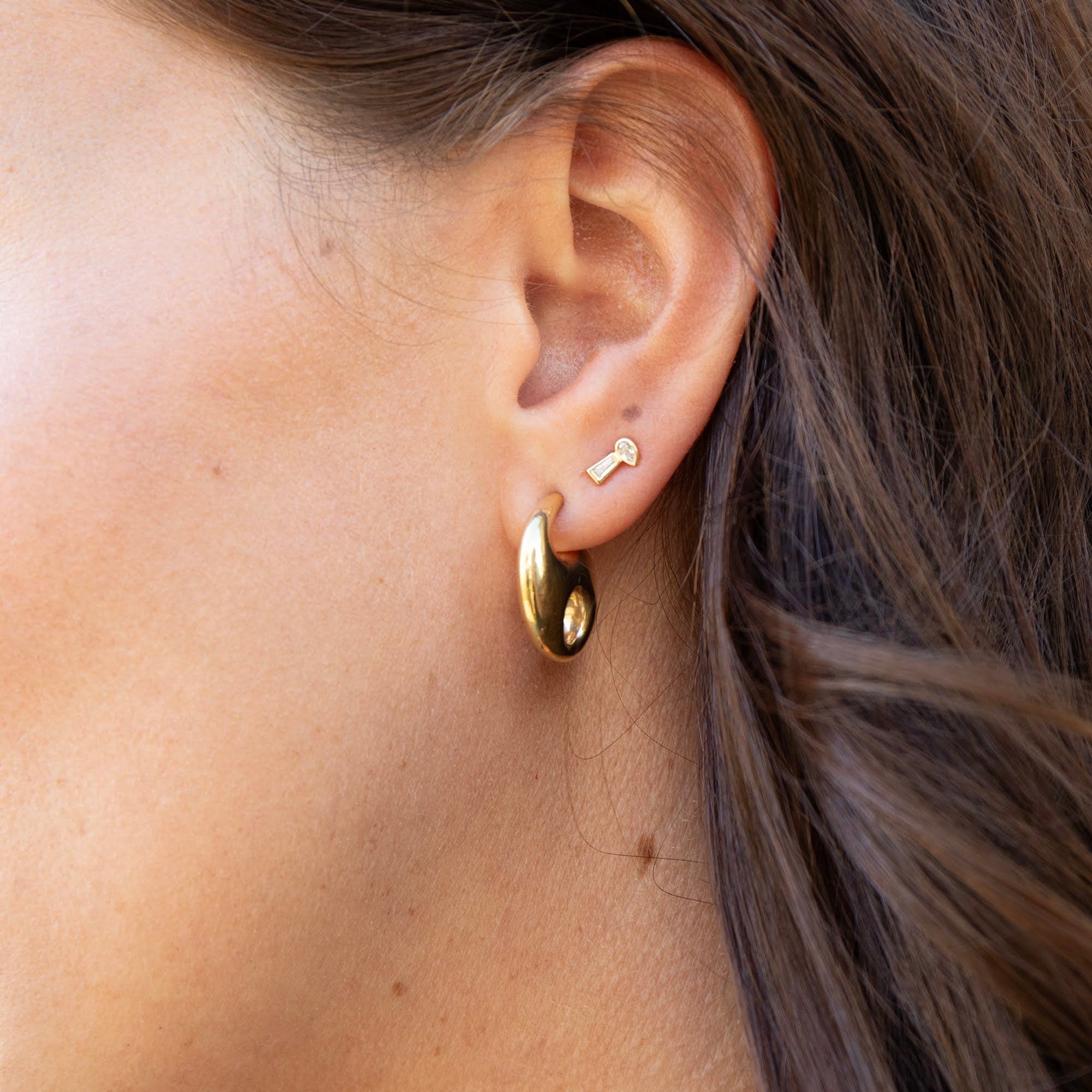 Close-up of an ear wearing a gold hoop earring with a small lock charm - tiny solid gold stud earring - seolgold