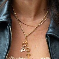 Gold necklace with 'P' and 'T' charms worn by a person in a black leather jacket  seolgold