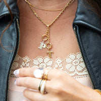 Gold necklace with letter charms worn by a person, close-up on a lace garment - seolgold
