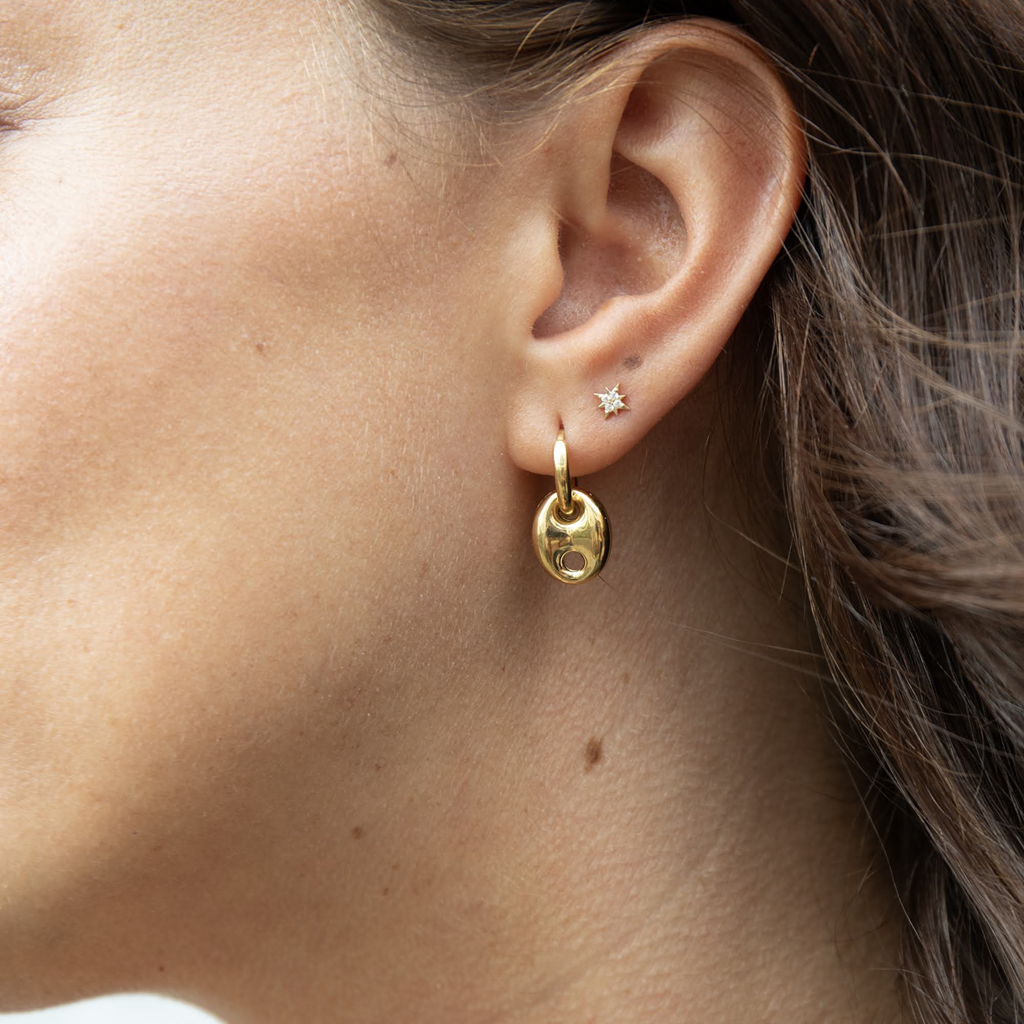 Close-up of a person wearing gold hoop earrings with a star-shaped stud - seolgold