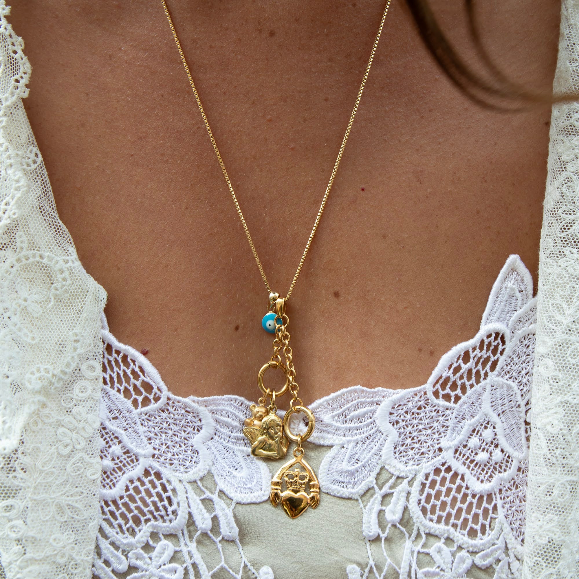 Gold necklace with charms on a person wearing a white lace garment - gold box chain - seolgold