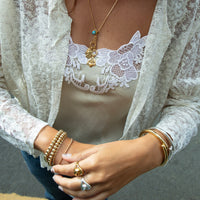 Person wearing a white lace top with gold jewelry and a gray background - Seol Gold