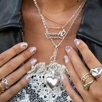 Person wearing layered silver necklaces with a heart pendant, surrounded by hands with rings and nail polish - seolgold