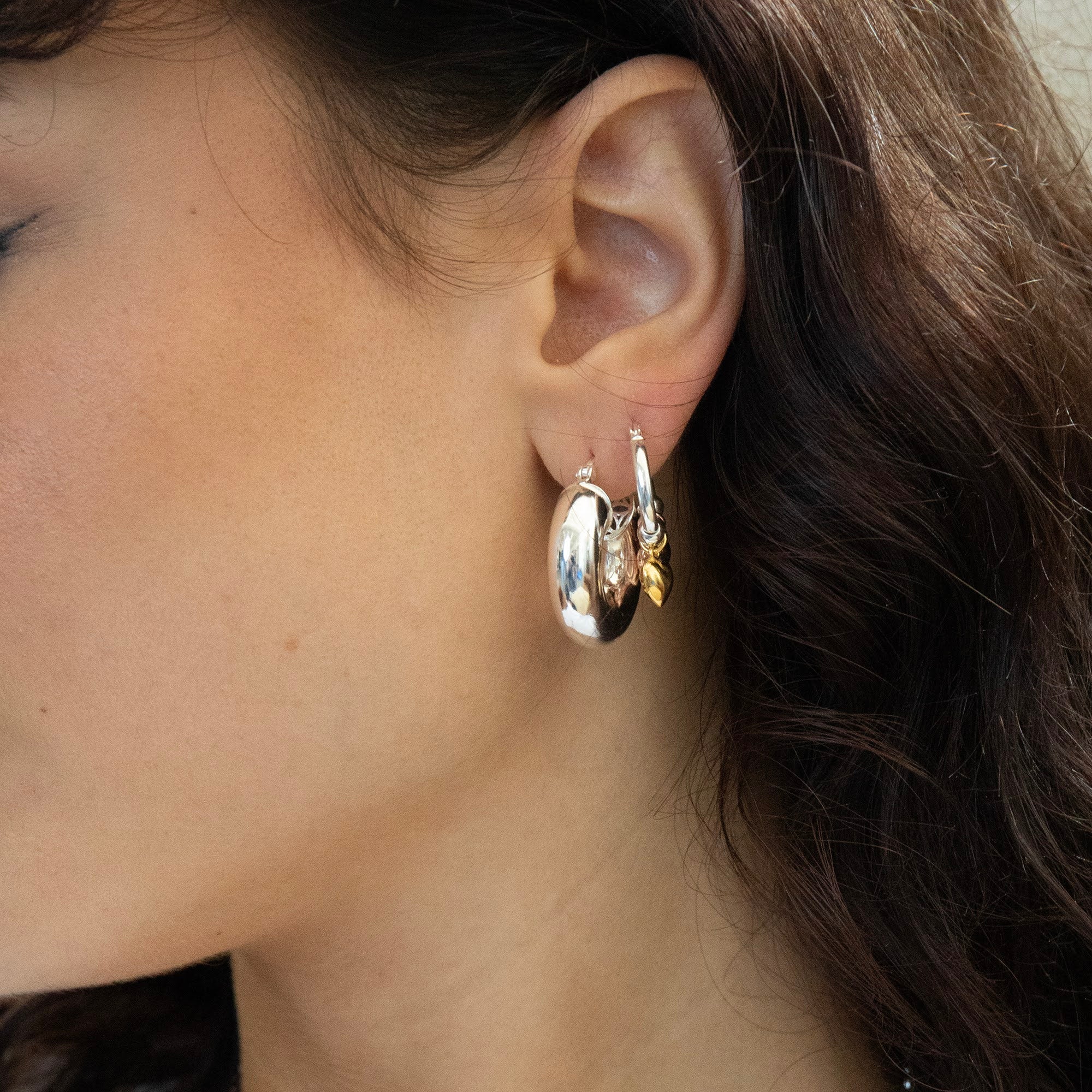 Close-up of an ear wearing a set of hoop earrings with a neutral background - Seol Gold 