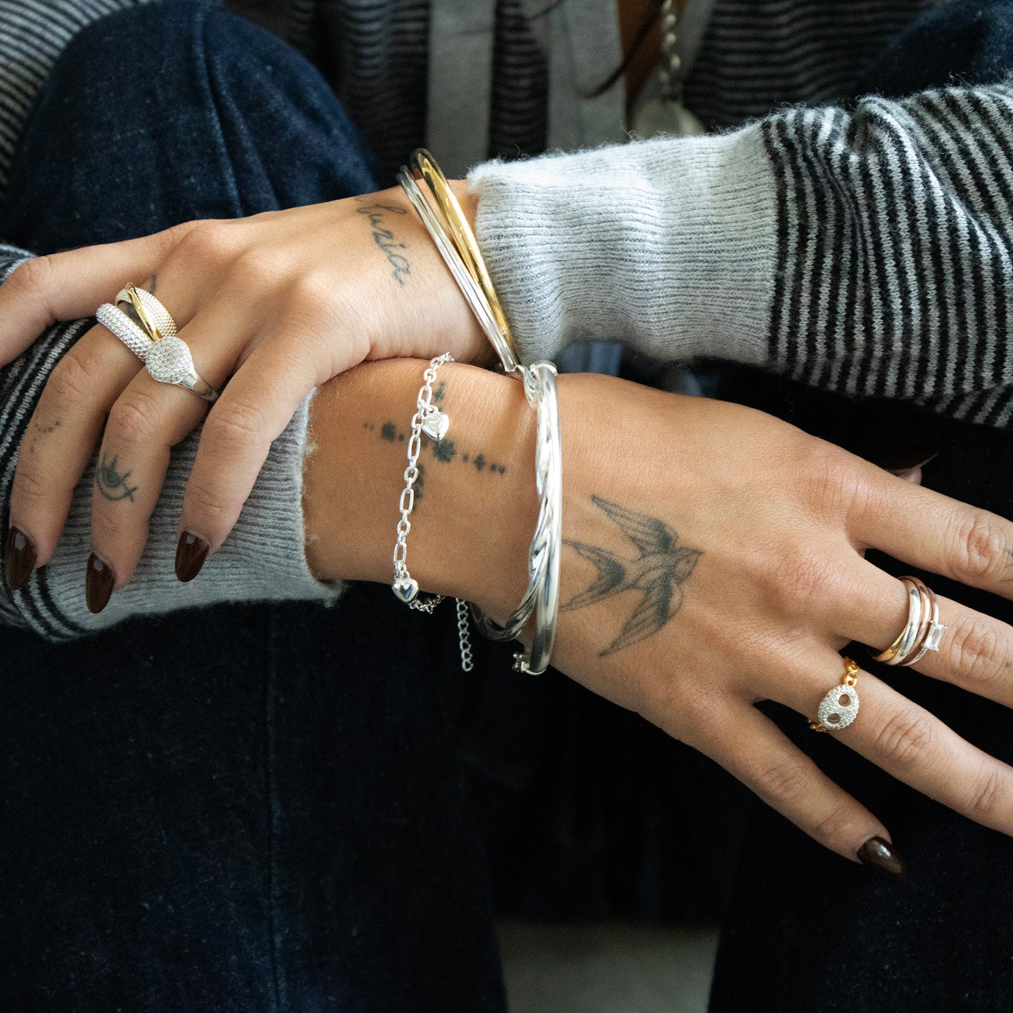 Close-up of a person's hands with multiple bracelets and rings on a dark background - Seol Gold
