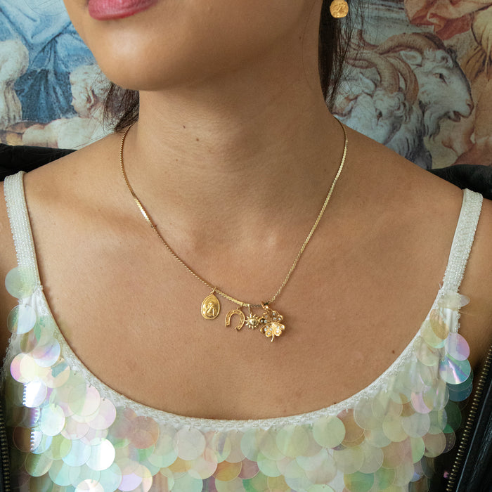 Gold necklace with charms worn by a person in front of a decorative background - seolgold