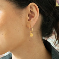 Close-up of a person wearing a gold hoop earring with a small round pendant - seolgold