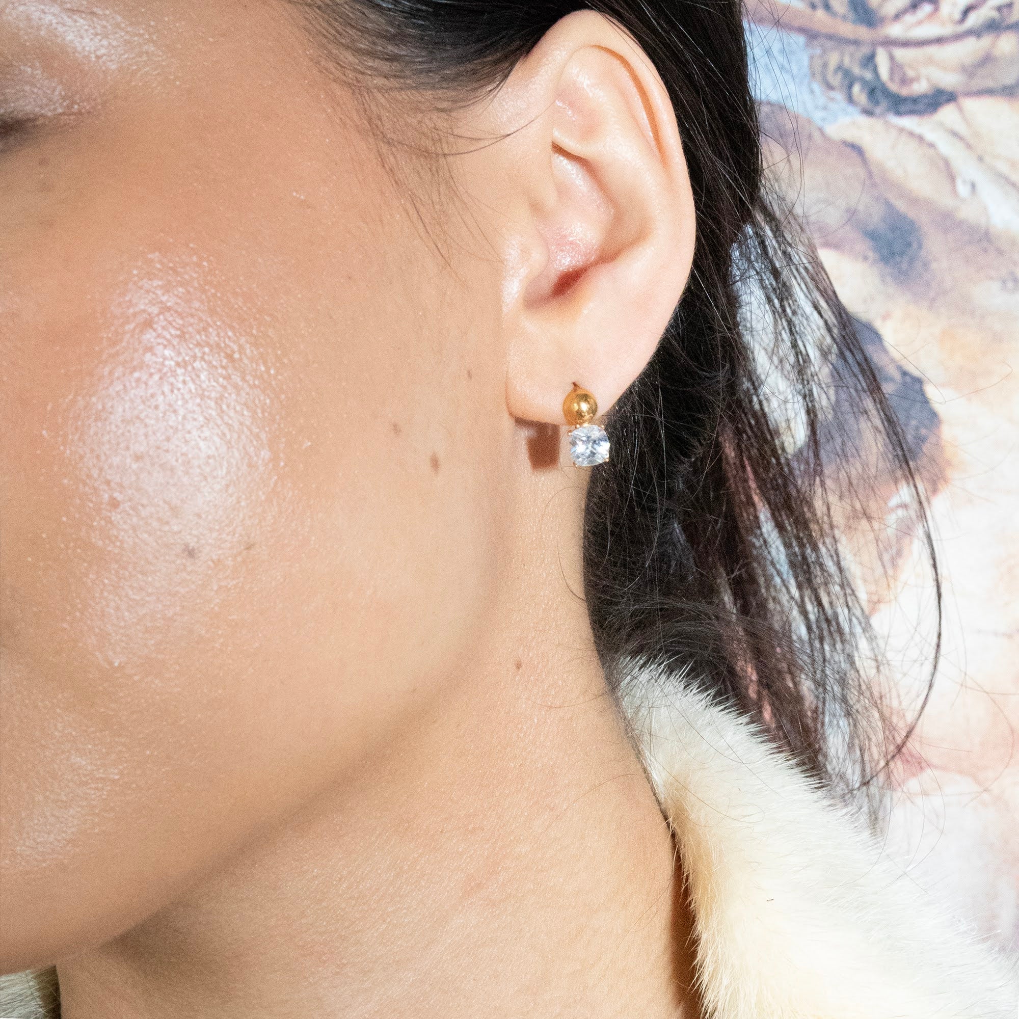 Close-up of a person wearing gold earrings with a clear gemstone - seolgold