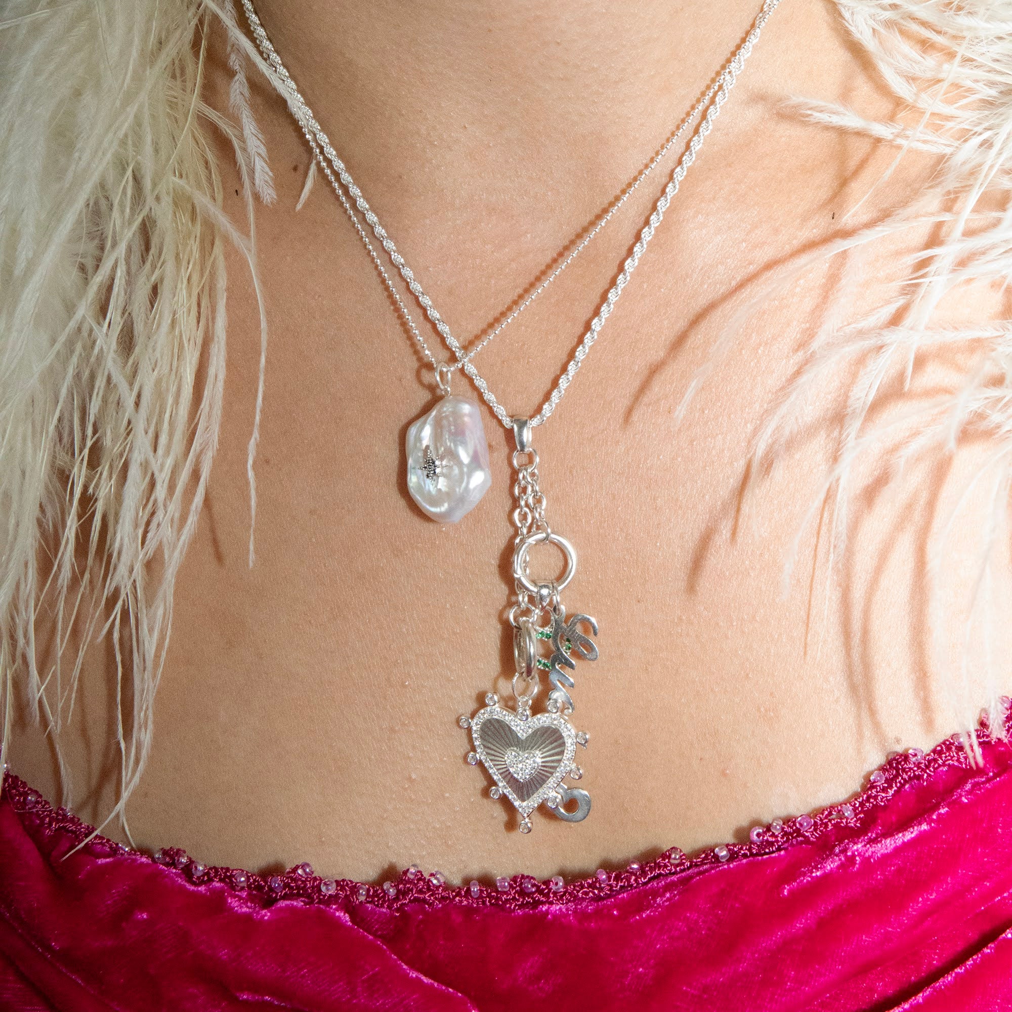 Silver necklace with heart pendant on a person wearing a pink top and feathered garment - seolgold