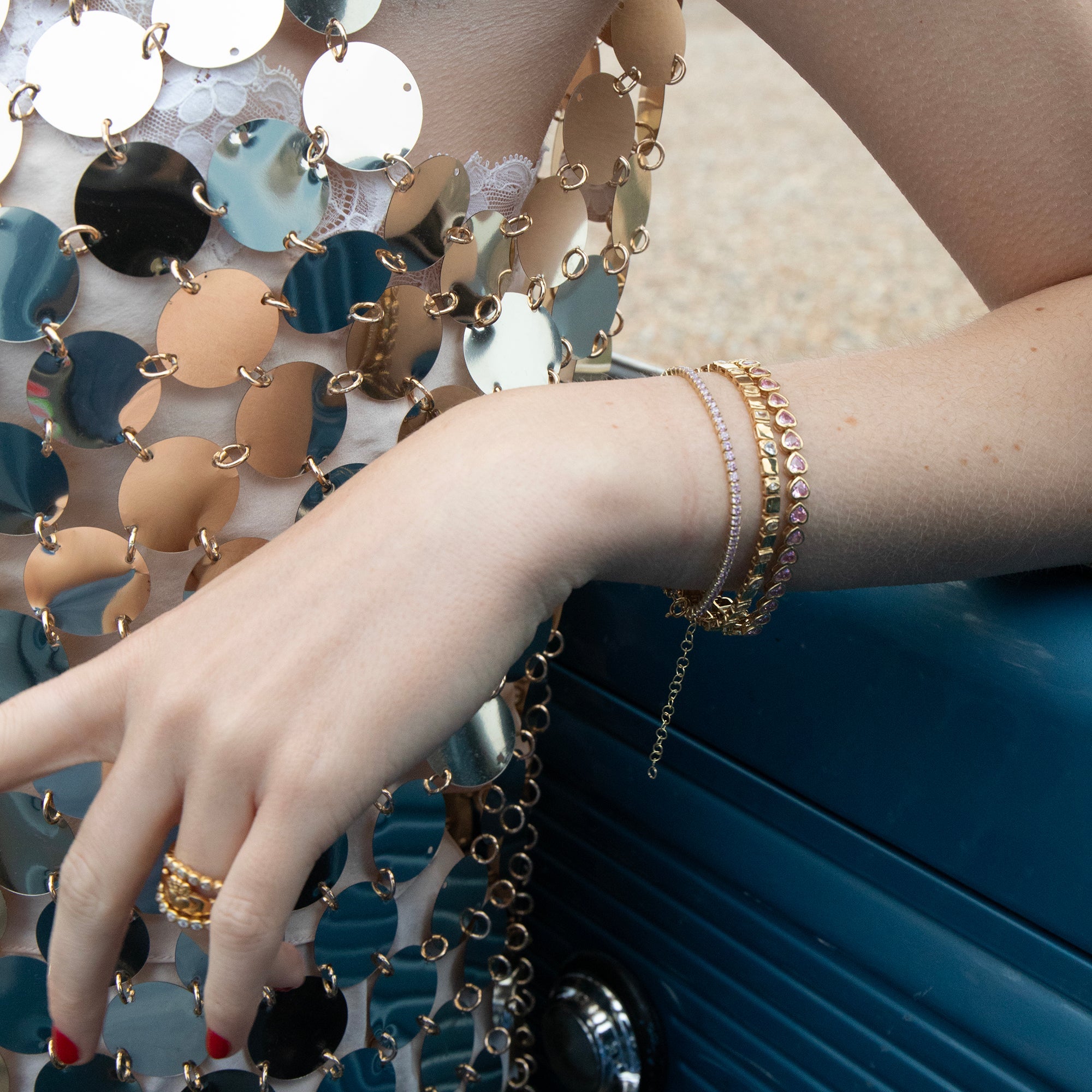 Close-up of a hand wearing gold bracelets with a colorful chainmail garment - seolgold