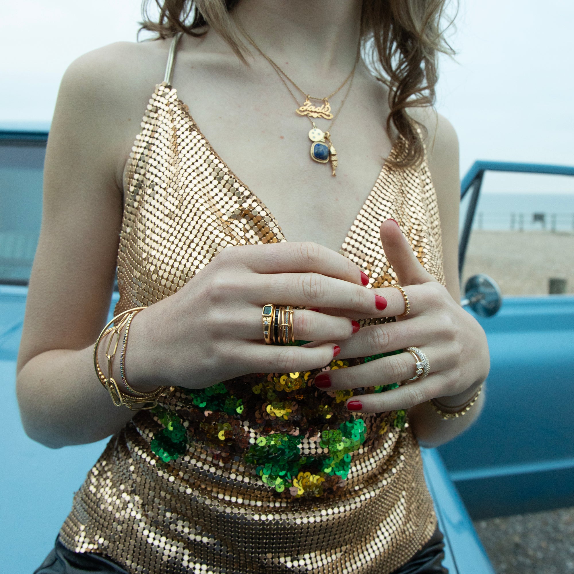 Woman wearing a gold sequin top and multiple pieces of jewelry with a blurred background - seolgold