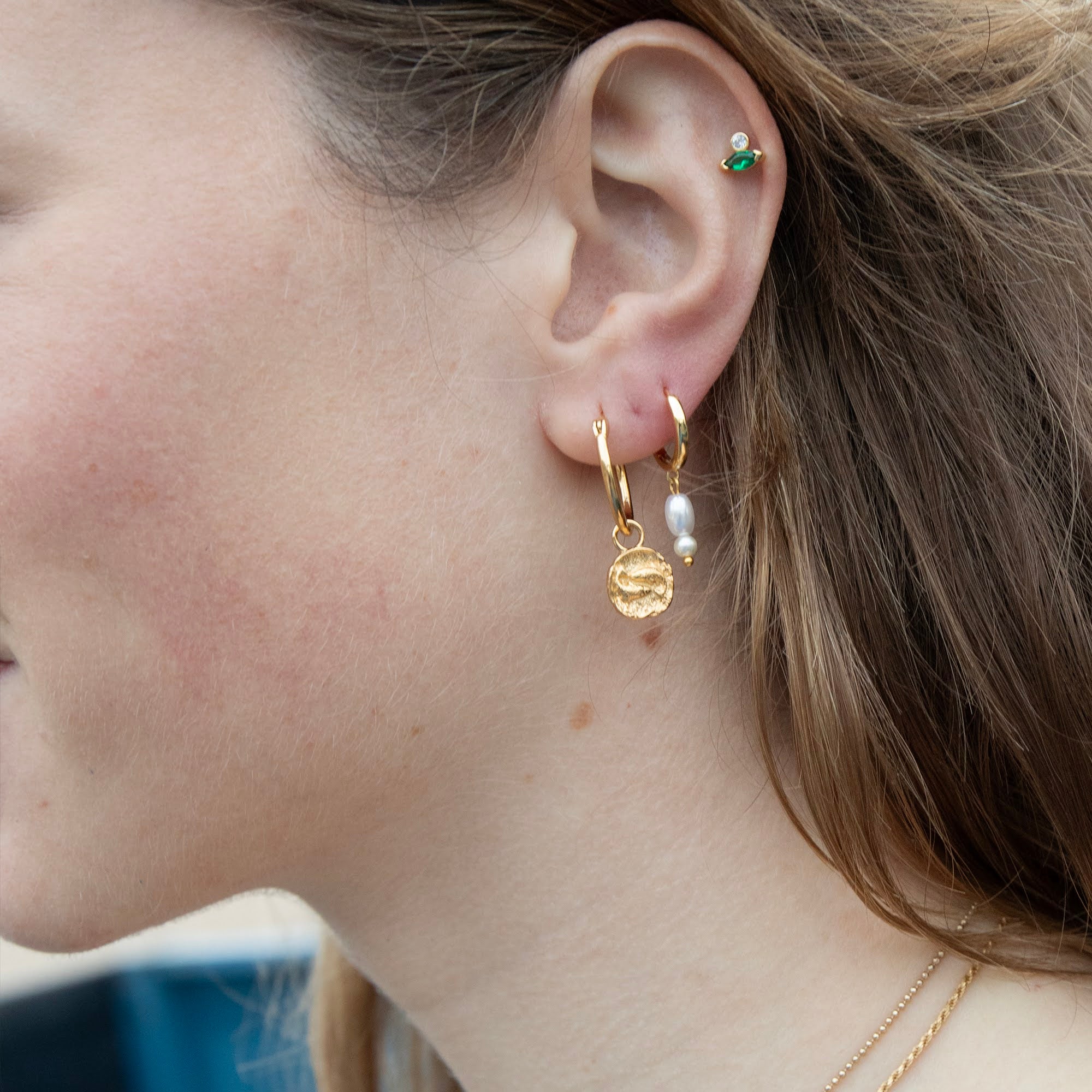 Close-up of a person's ear wearing gold hoop earrings with small charms - seolgold