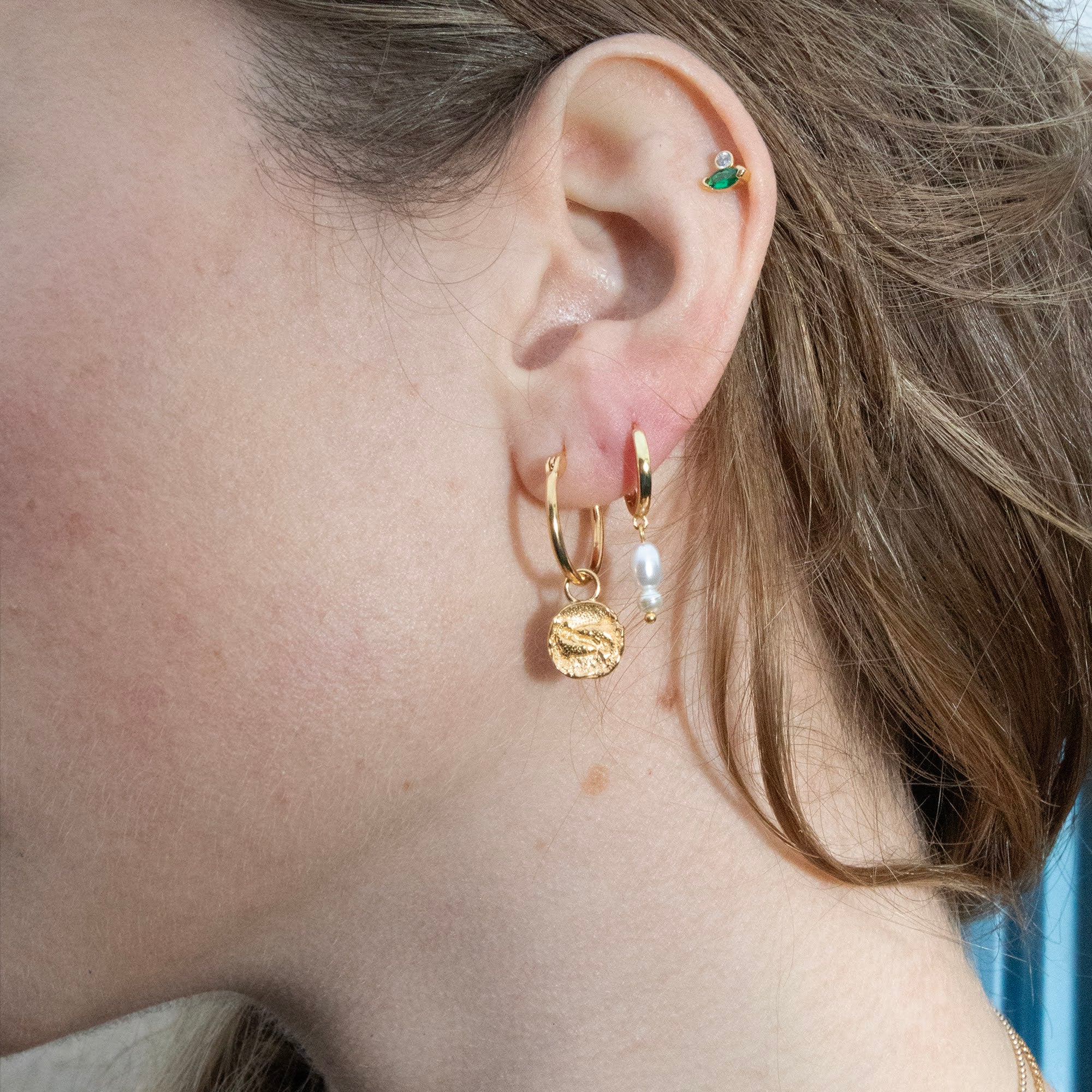 Close-up of an ear with gold hoop earrings and a small green gemstone earring - seolgold