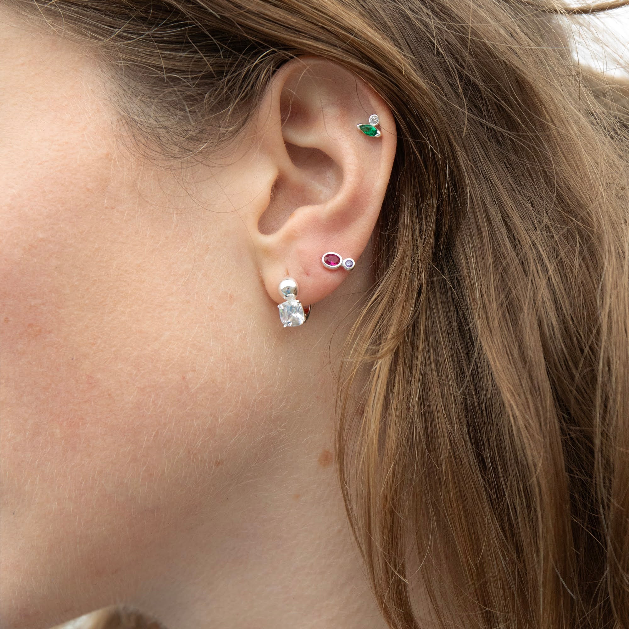 Close-up of an ear wearing multiple silver and gemstone earrings with a blurred background - seolgold