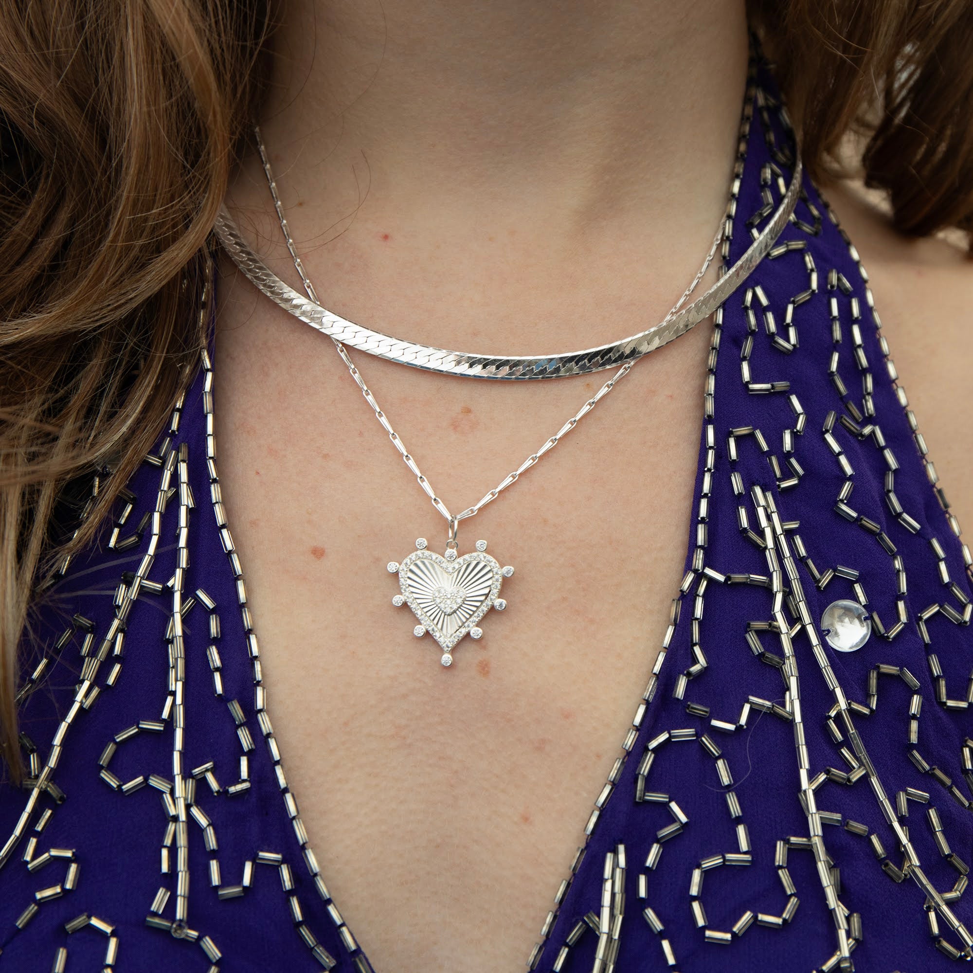 Silver heart-shaped necklace worn by a person with a blue embroidered garment - seolgold