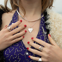 Close-up of a hand wearing multiple silver rings and bracelets on a black leather surface - seolgold