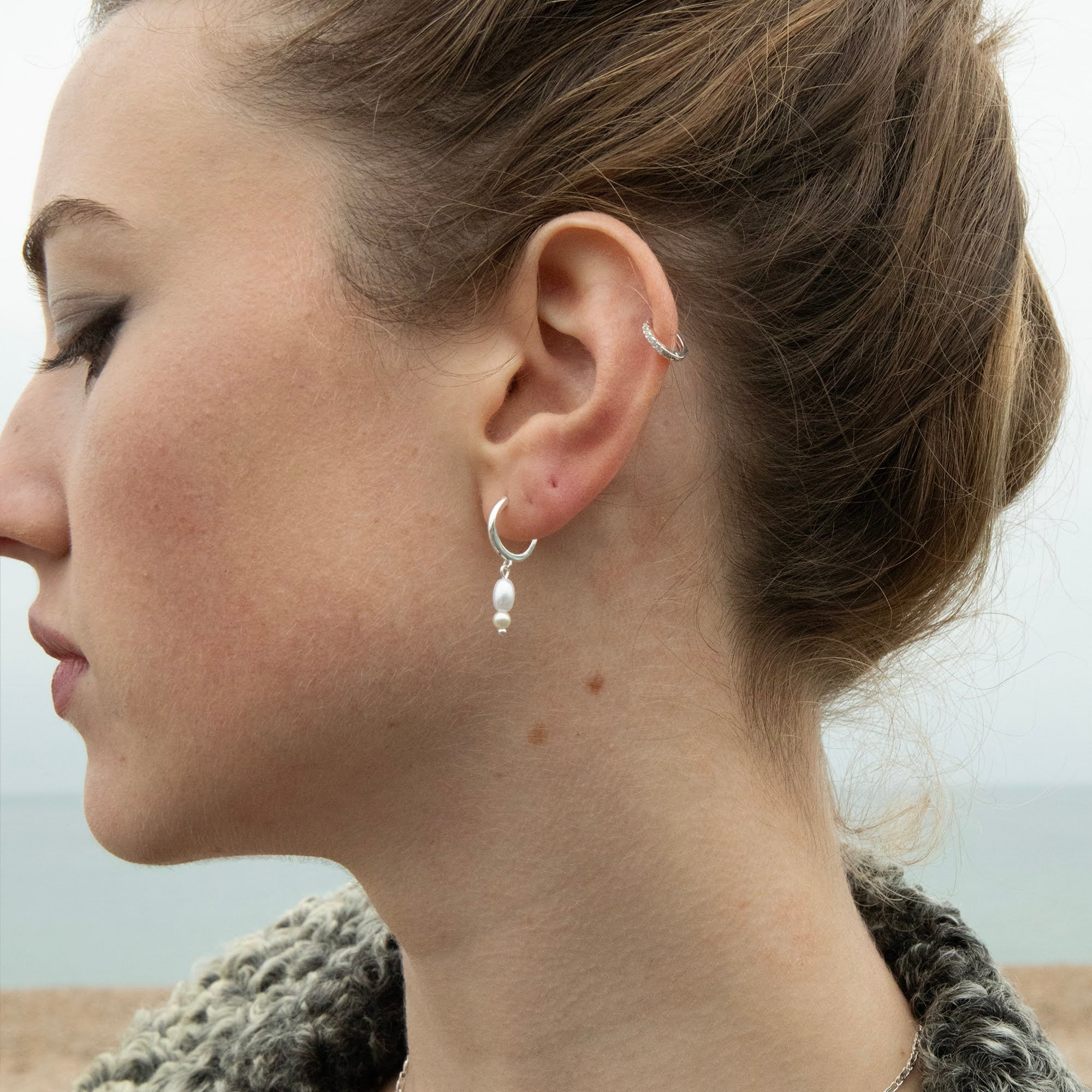 Close-up of a woman's ear wearing a silver earring with a blurred background - seolgold