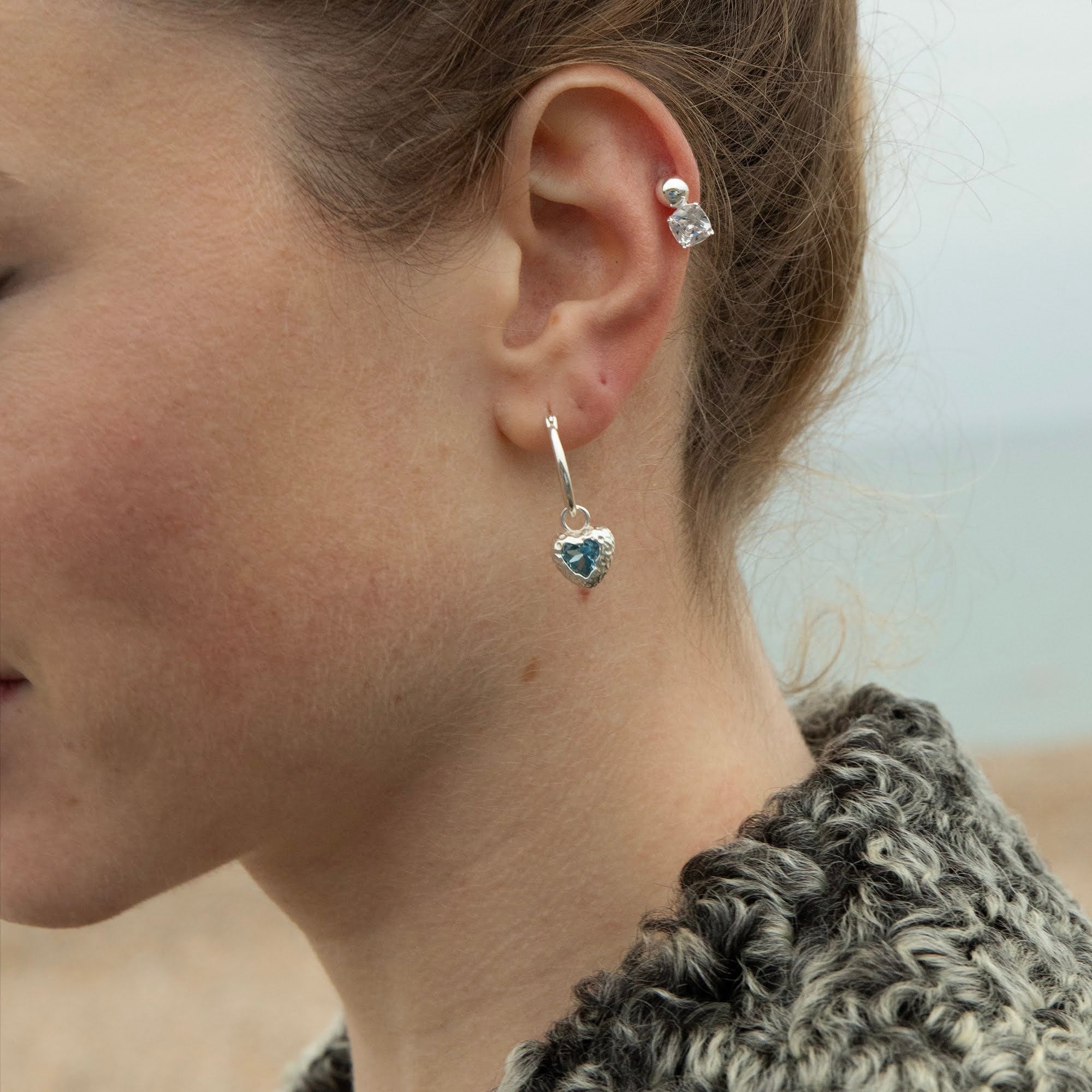Close-up of a person wearing heart-shaped earrings with a blurred background - seolgold