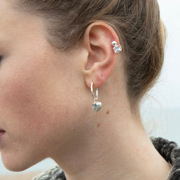 Close-up of a person wearing silver hoop earrings with heart charms - seolgold