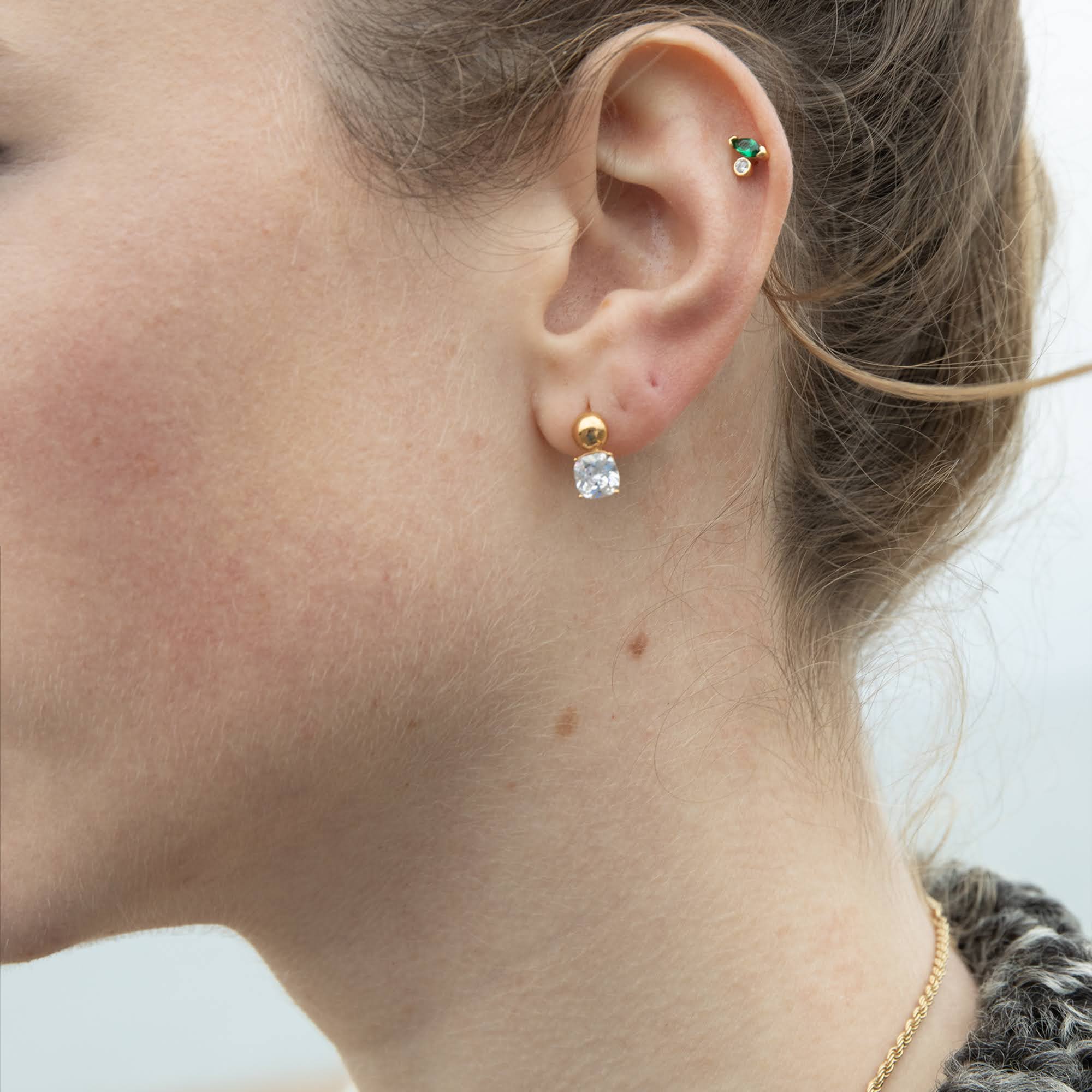 Close-up of a person wearing gold and silver earrings with a blurred background - seolgold