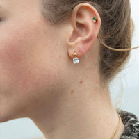 Close-up of a person wearing gold and silver earrings with a blurred background - seolgold