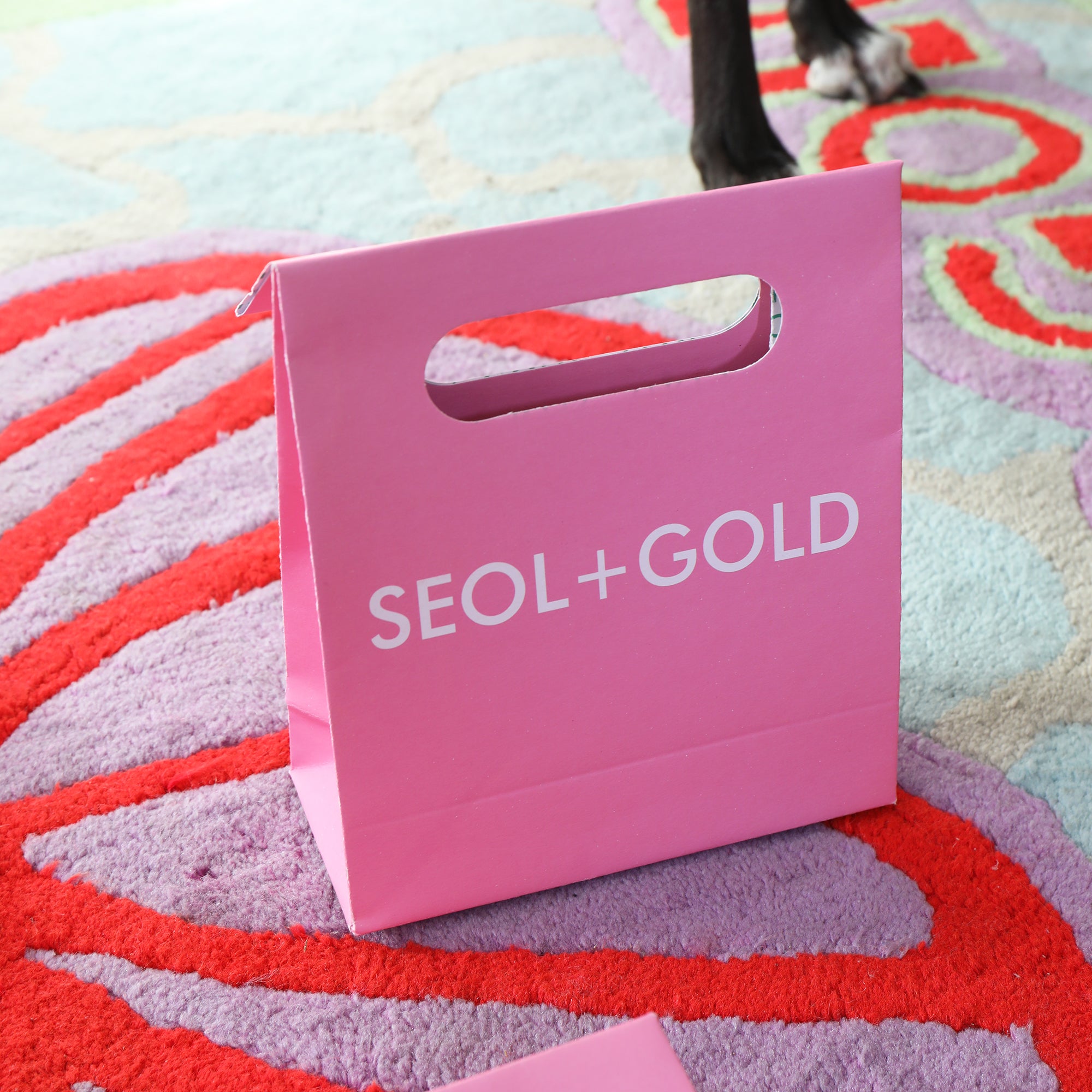 Pink 'SEOL+GOLD' bag on a colorful patterned carpet - seolgold